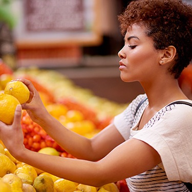 IMAGE: Woman comparing citrus fruit in grocery store.