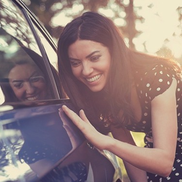 a woman smiling touching her new car