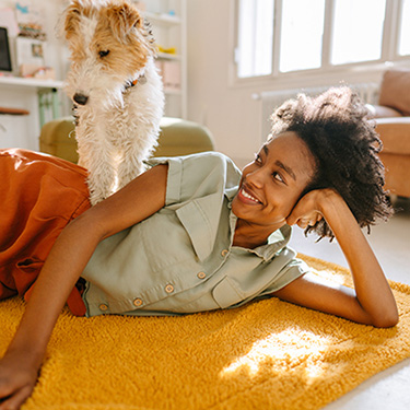 IMAGE: Woman laying on her side on the floor with small dog sitting on her hip.