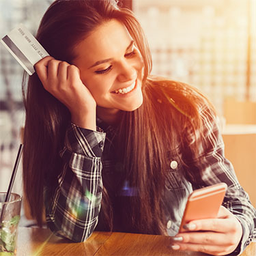 IMAGE: Young woman holding debit card in one hand looking at phone in other hand