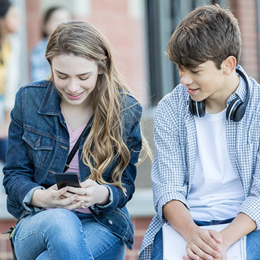 IMAGE: Two teens looking at phone together and smiling