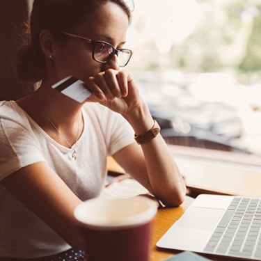 a woman holding her credit/debit card thinking of a purchase.