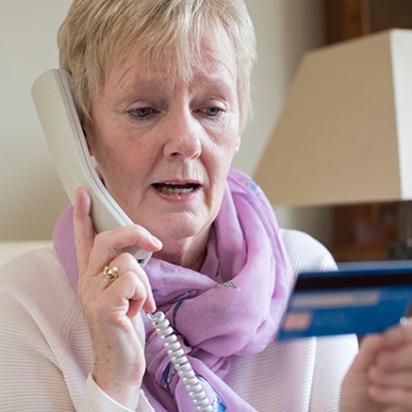 an elderly woman on a phone holding a debit/credit card.