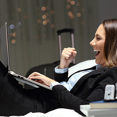 IMAGE: Business woman in hotel, cheering at computer screen.