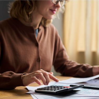 IMAGE: Woman using a calculator while sitting at desk with paperwork