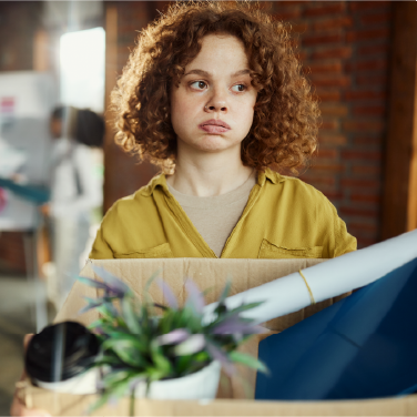 IMAGE: Woman holding box of desk items with worried expression