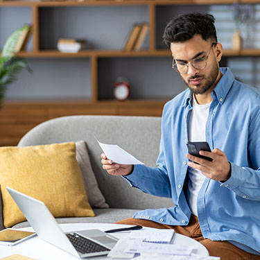 IMAGE: Man holding phone and paper looking concerned