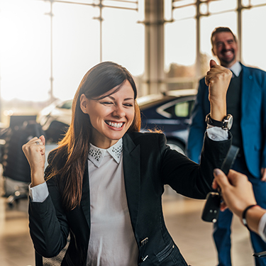 IMAGE: Woman celebrating in a car dealership and being handed keys