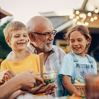 IMAGE: Grandfather hugging grandkids outside at a BBQ