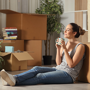 IMAGE: Woman sitting on floor in house with boxes and cup of coffee