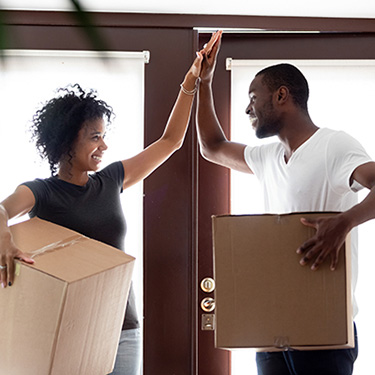 IMAGE: Couple high-fiving with moving boxes in entryway to home.