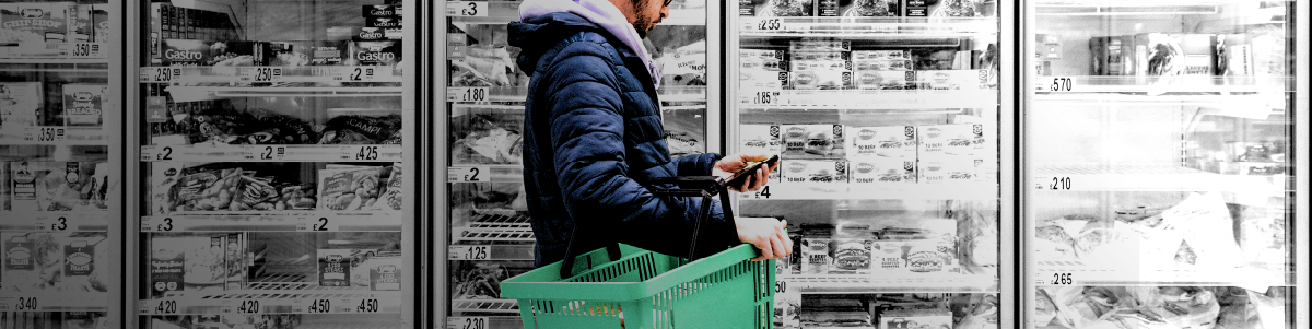 IMAGE: Man holding phone and basket in a grocery story aisle.