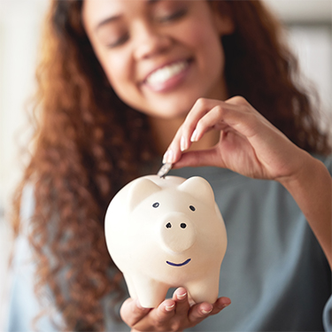 IMAGE: Young woman smiling while placing coin in piggy bank