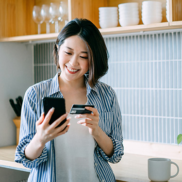 IMAGE: Woman holding phone and credit card in kitchen