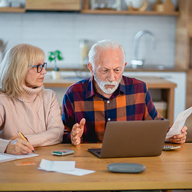 IMAGE: Older adults looking confused at a laptop at a kitchen table.