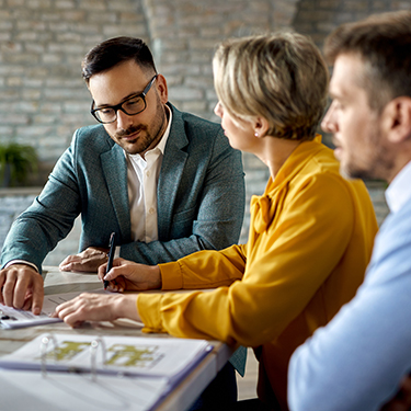 IMAGE: Couple talking with real estate agent and signing paperwork