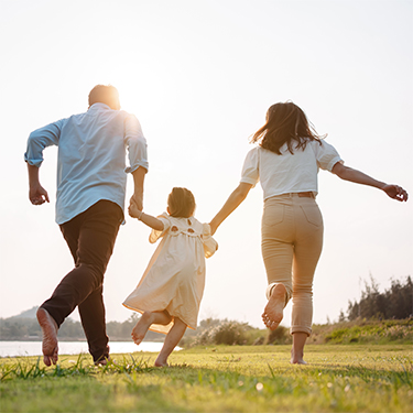 IMAGE: Family walking barefoot in a field on a sunny day and holding hands