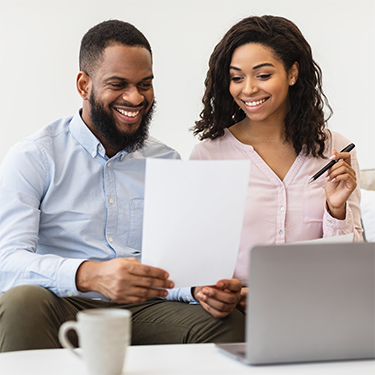 IMAGE: Couple smiling looking at paper and laptop