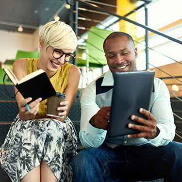 IMAGE: Woman and man sitting on stairs in office smiling and reviewing notes.