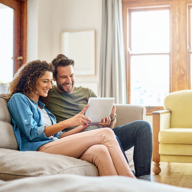 IMAGE: Couple sitting on a couch and holding tablet smiling