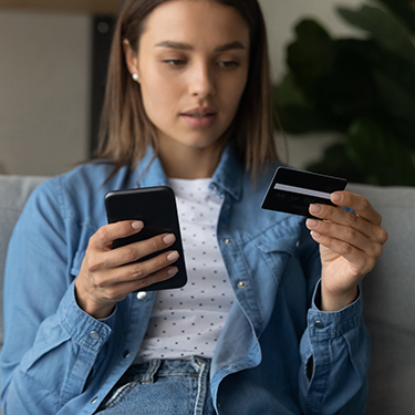 IMAGE: Woman looking concerned holding credit card and cell phone