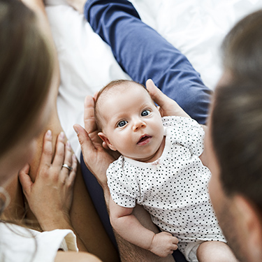 IMAGE: Newborn in parent's lap looking up at the camera