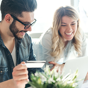 IMAGE: Smiling couple looking at a laptop while man holds a credit card