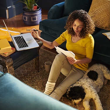 IMAGE: Woman sitting next to dog on floor in home looking at papers with laptop open