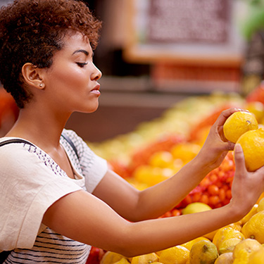 IMAGE: Woman comparing citrus fruit in grocery store.