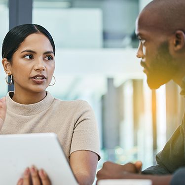 IMAGE: Two coworkers looking concerned talking with laptop open