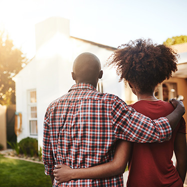 IMAGE: Couple standing outside looking towards front of house.