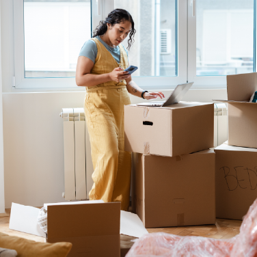 IMAGE: Woman in process of moving homes with laptop and phone open