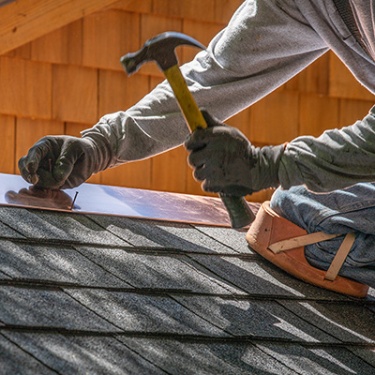 a construction worker nailing shingles in a roof