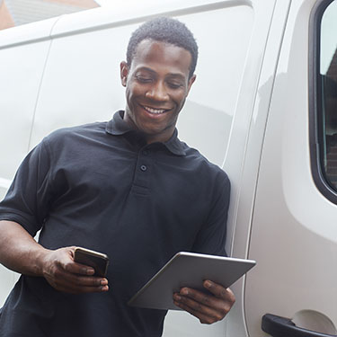 IMAGE: Man holding tablet and phone while leaning on commercial vehicle